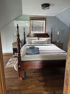 Een slaapkamer met een hemelbed, een houten hoofdbord, een nachtkastje met een lamp en een raam met jaloezieën.