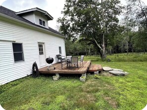 Ein weißes Haus mit einer Holzdiele, Gartenmöbeln und einem Grill.