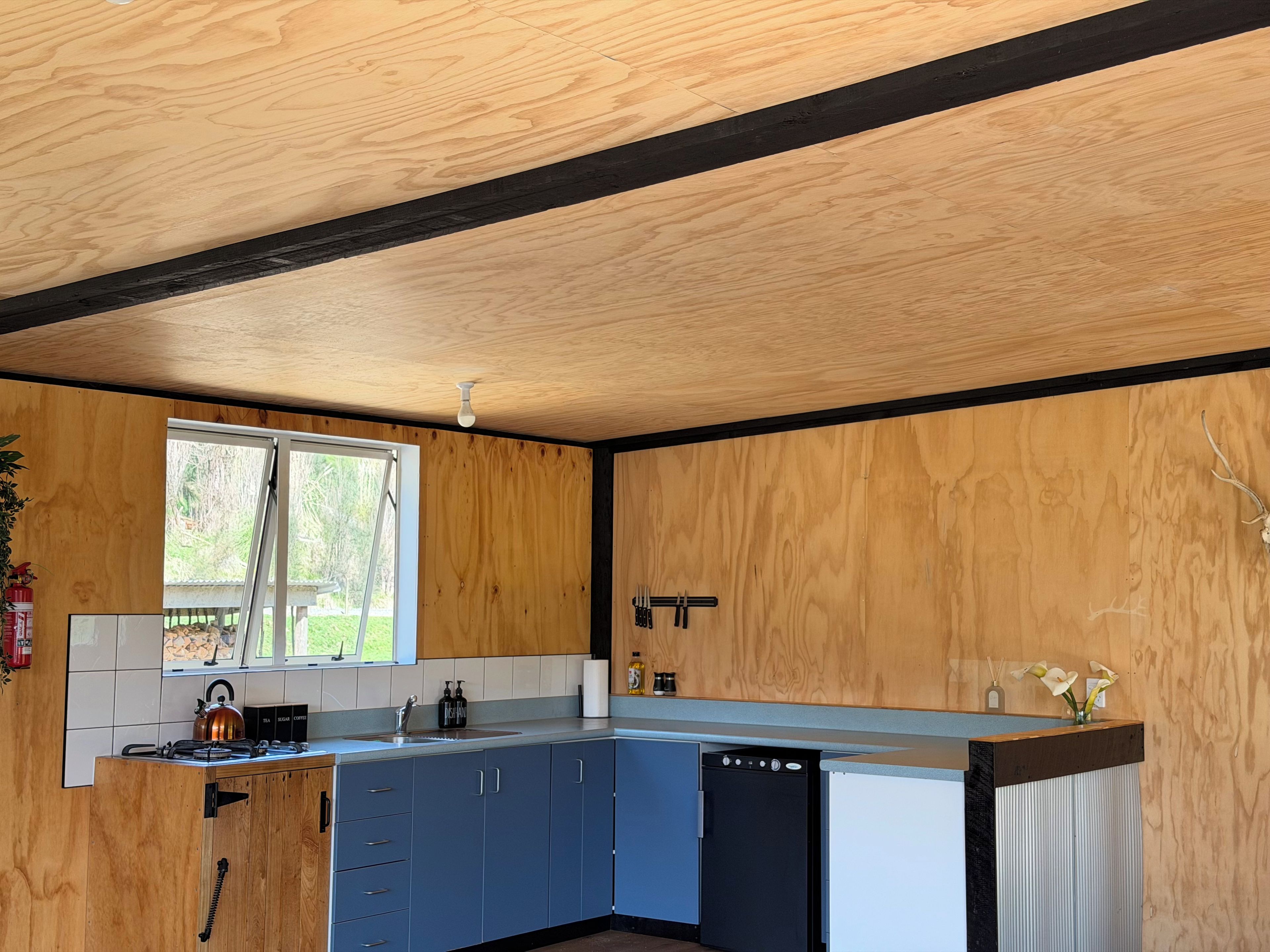 A kitchen with wooden walls, a window, a sink, cabinets, and a dishwasher.
