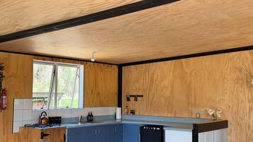A kitchen with wooden walls, a window, a sink, cabinets, and a dishwasher.