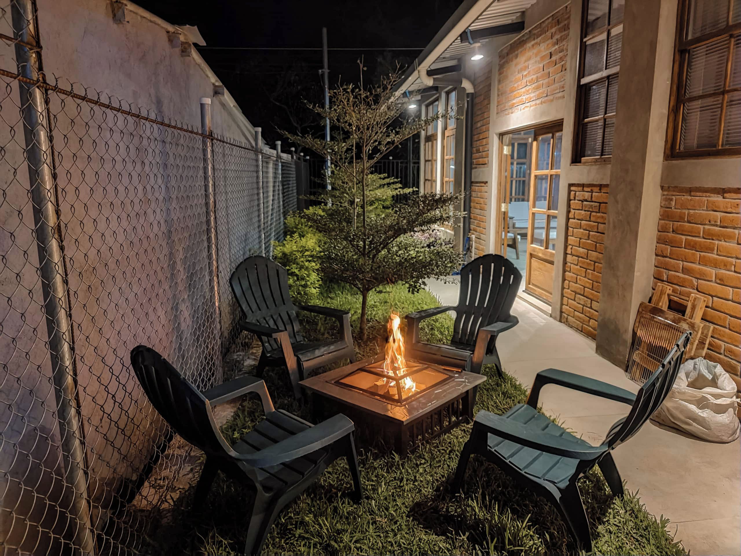 Une terrasse avec un foyer, quatre chaises et un petit arbre.