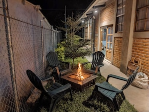 Un patio con un brasero, cuatro sillas y un pequeño árbol.