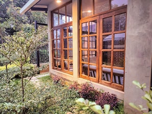 A building with large windows and a garden area with various plants. - Modern Coffee Farm House in Ruta de las Flores (Sonsonate)