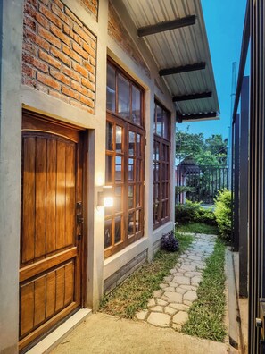A building with a brick facade, large wooden doors, and a stone pathway leading to a gated entrance. - Modern Coffee Farm House in Ruta de las Flores (Sonsonate)