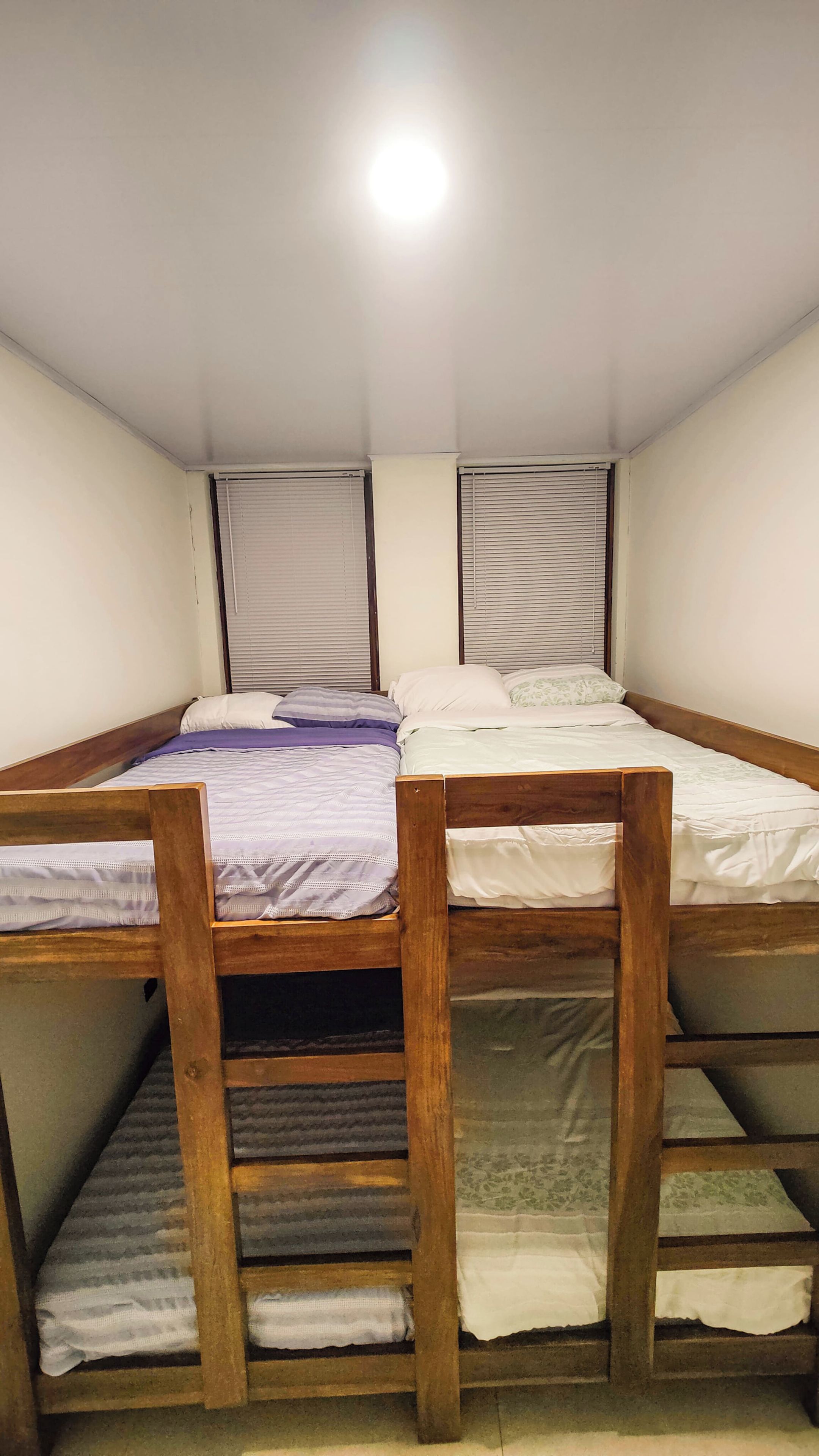 A bunk bed room with a wooden headboard, a single bed with a white mattress, and a window with blinds.