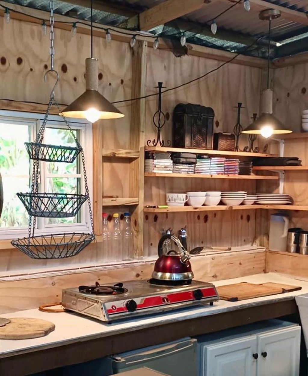 Una cocina rústica con paredes de madera, lámparas colgantes y repisas con vajilla y libros.