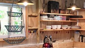 Una cocina rústica con paredes de madera, lámparas colgantes y repisas con vajilla y libros.