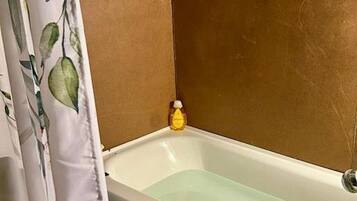 Un baño con bañera, cortina de ducha y una botella de champú.