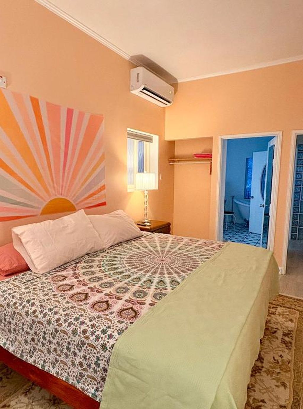 Un dormitorio con cama, aire acondicionado de pared, ventana y puerta que da a otra habitación.
