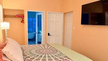 Un dormitorio con cama, televisión y puerta que da a un baño.