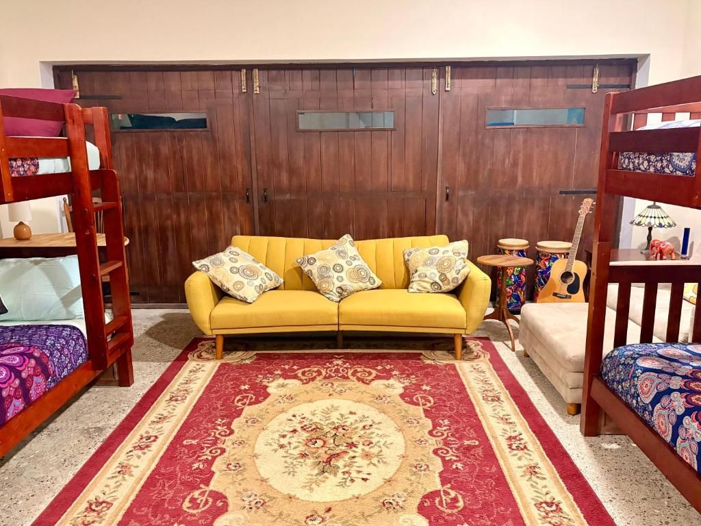 A room with a yellow sofa, a red and beige patterned rug, a wooden door, and a guitar on a side table.
