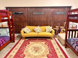 Una habitación con un sofá amarillo, un tapete de diseño rojo y beige, una puerta de madera y una guitarra sobre una mesita.