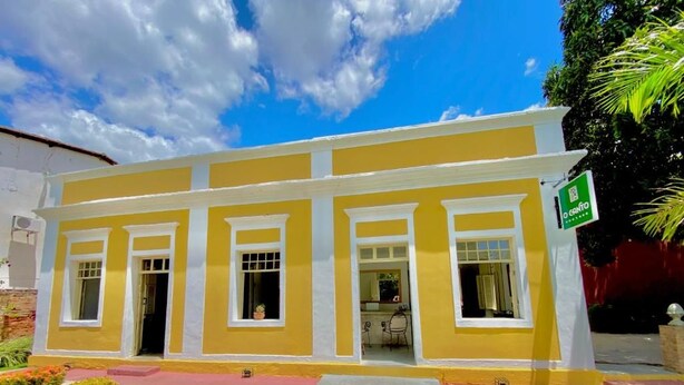 A yellow building with a green sign, a paved entrance, and a well-maintained lawn. - O Canto Pousada (Piranhas)