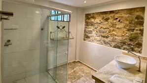 A bathroom with a glass-enclosed shower, a stone wall, and a marble sink. - O Canto Pousada (Piranhas)