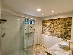 Ein Badezimmer mit einer gläsernen Duschkabine, einer Steinwand und einem мраморном Waschbecken.
