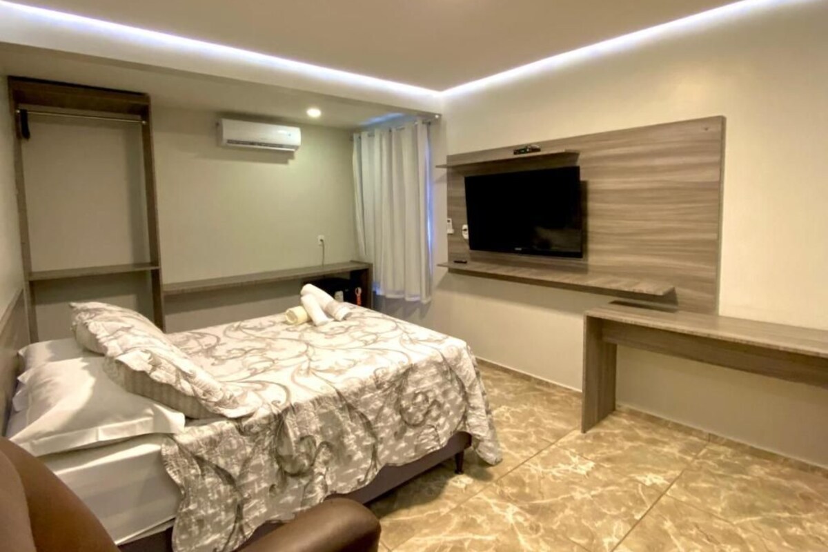 Ein Schlafzimmer mit einem Bett, einem an der Wand montierten Fernseher und einem Schreibtisch.