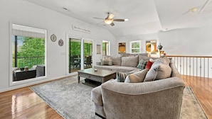 A spacious living room with a large gray sectional sofa, a coffee table, and a ceiling fan. There is a sliding glass door leading to an outdoor patio area. - Elevated VIEWS, Outdoorsy Vibe, Speakeasy Kg Suite (Leasburg)