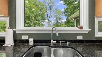 A kitchen with a double sink, a window with a view of trees, and a candle on the counter.