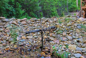 A natural outdoor area with a wooden structure, surrounded by a variety of rocks and greenery. - Penny's Peaceful Pines (Sevierville)