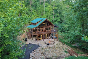 A two-story log cabin with a deck, surrounded by dense forest. - Penny's Peaceful Pines (Sevierville)