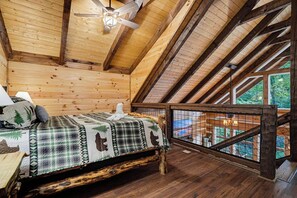 A wooden cabin bedroom with a bed, a ceiling fan, and a window overlooking a deck. - Penny's Peaceful Pines (Sevierville)