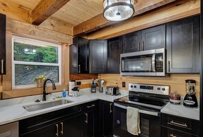 A modern kitchen with dark cabinetry, stainless steel appliances, and a window with a view of greenery. - Penny's Peaceful Pines (Sevierville)