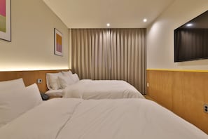 Habitación de hotel con dos camas, un televisor de pantalla plana montado en la pared y un ventanal con cortinas.