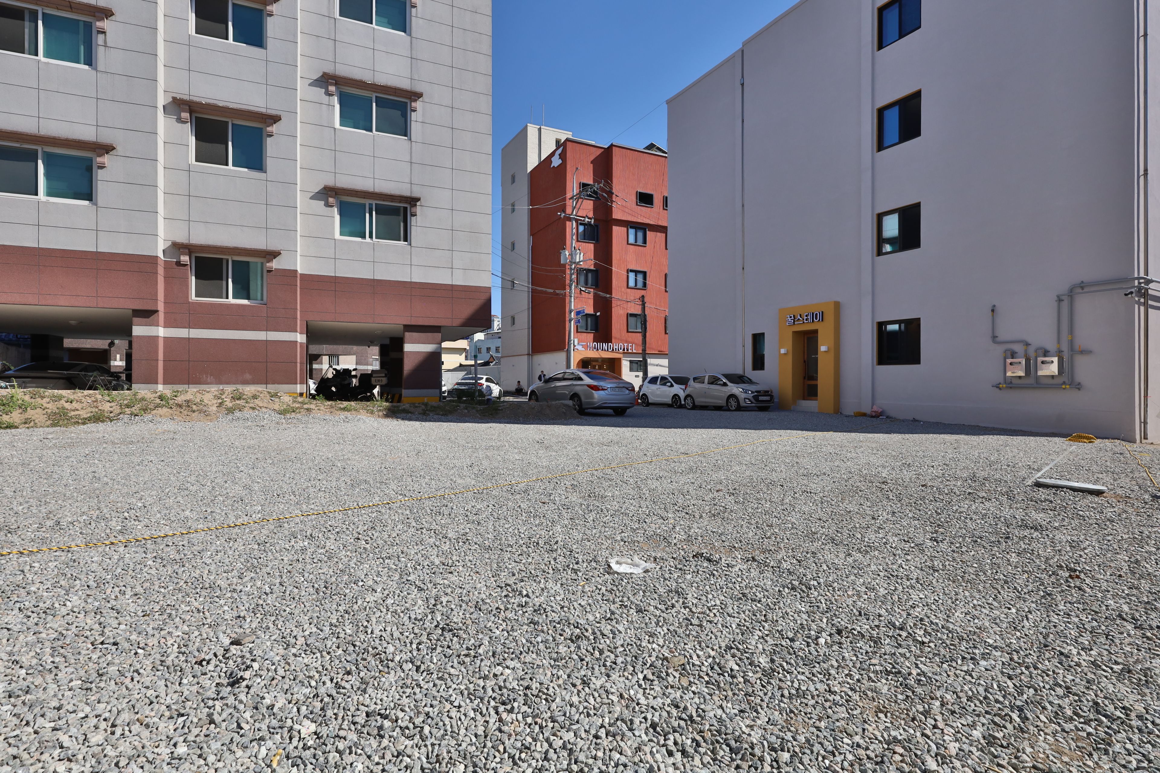 A parking area with multiple cars and a building with a red facade and a yellow door.
