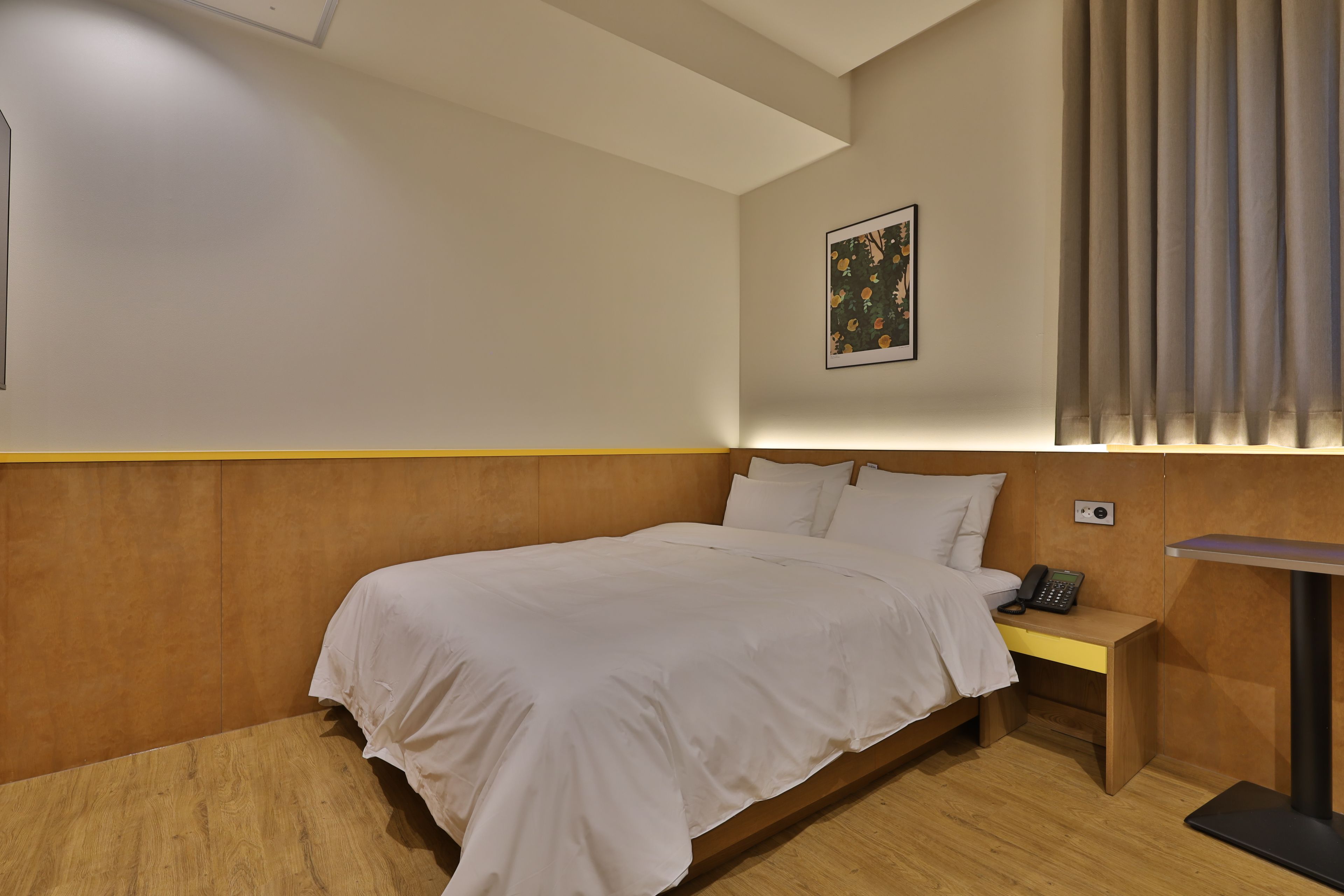 A hotel room with a bed, bedside table, and a wall-mounted phone.