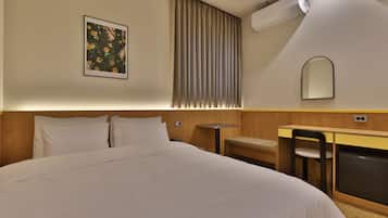 Habitación de hotel con cama, escritorio, silla, aire acondicionado, espejo y ventana con cortinas.