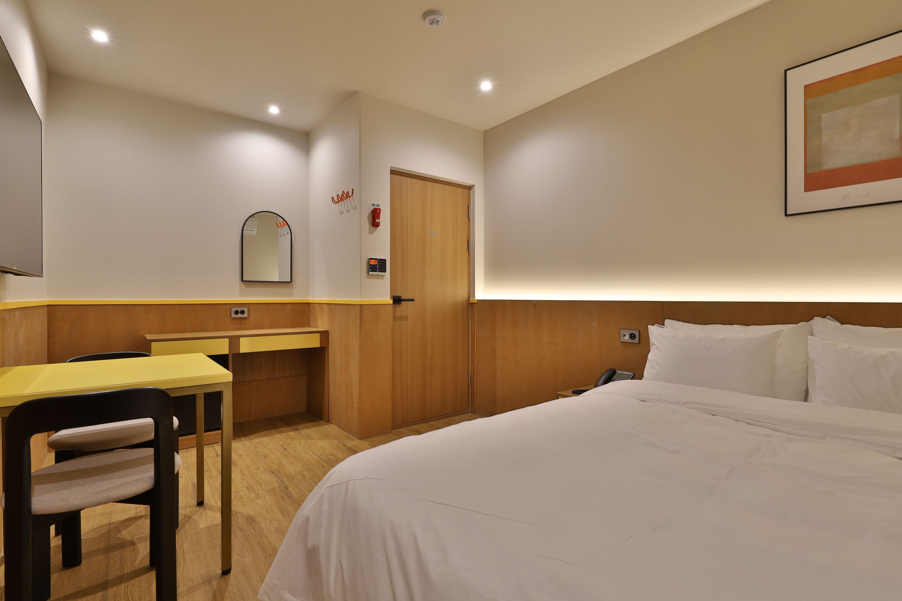 Ein Hotelzimmer mit Bett, Schreibtisch, Stuhl, Spiegel und Tür.