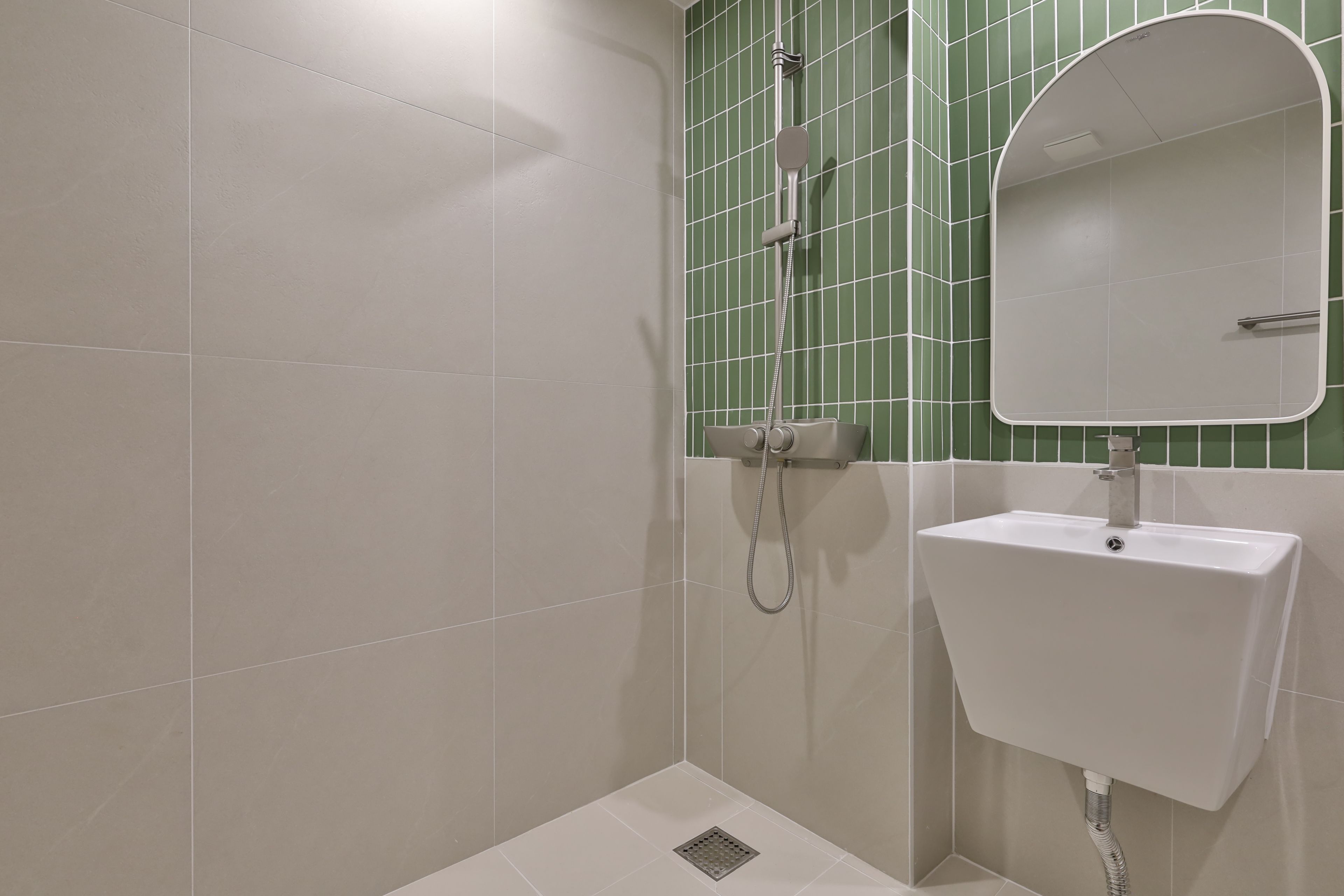 Un baño con lavamanos blanco, un espejo y una ducha con pared de azulejos verdes.