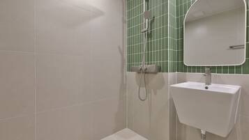 Un baño con lavamanos blanco, un espejo y una ducha con pared de azulejos verdes.