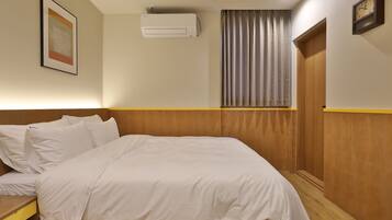 Ein Hotelzimmer mit einem Bett, einem Nachttisch, einer Wandklimaanlage, einem gerahmten Bild und einer Uhr.