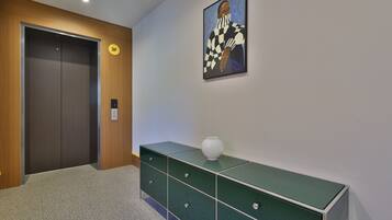 Un pasillo con una puerta de madera, un mueble de almacenamiento verde, un jarrón blanco y un cuadro en la pared.