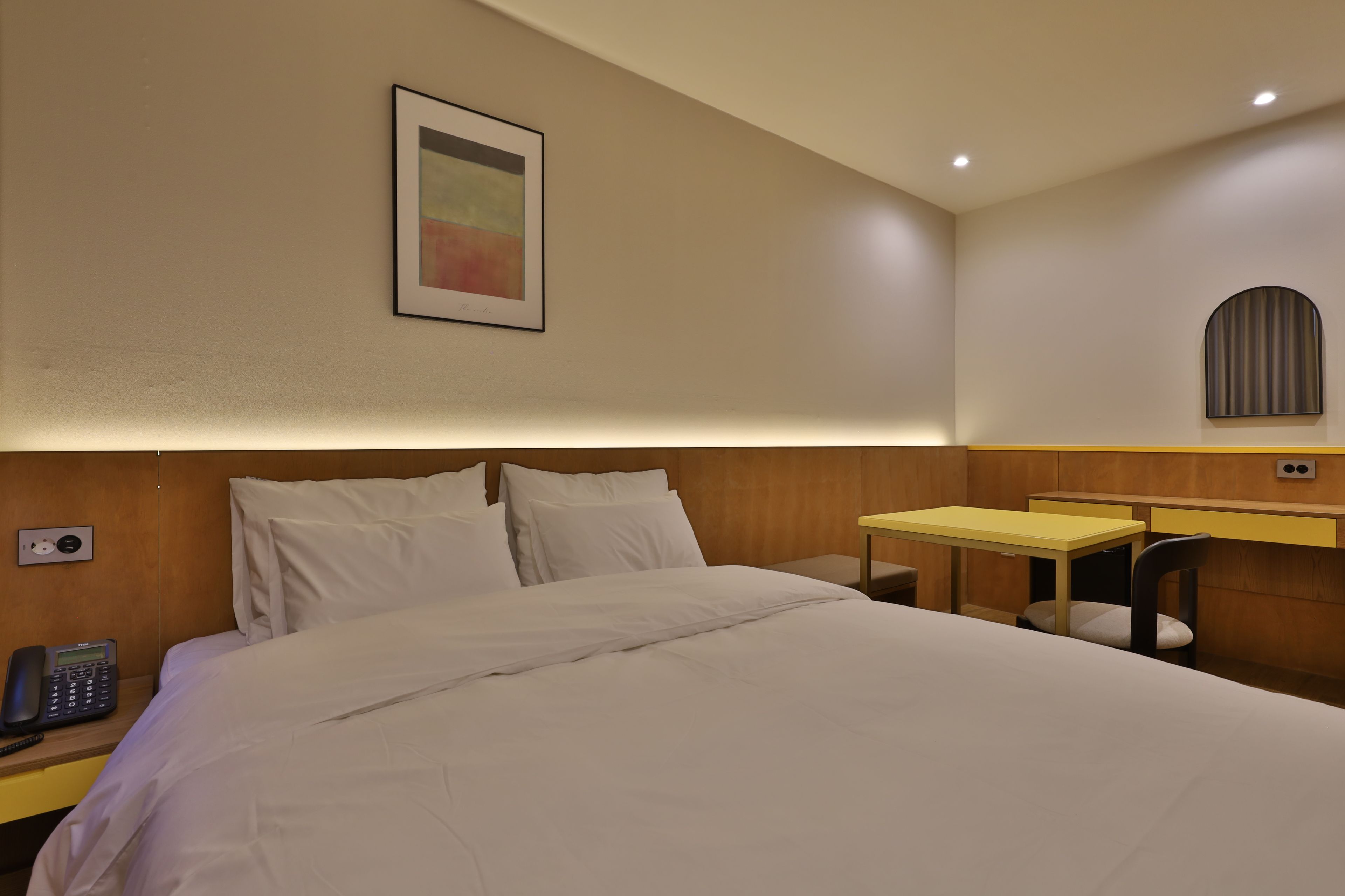 A hotel room with a bed, bedside table, a desk, and a chair.