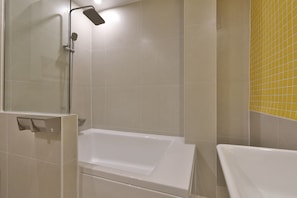 Un baño con ducha envuelta en vidrio, una bañera blanca y paredes con azulejos amarillos.