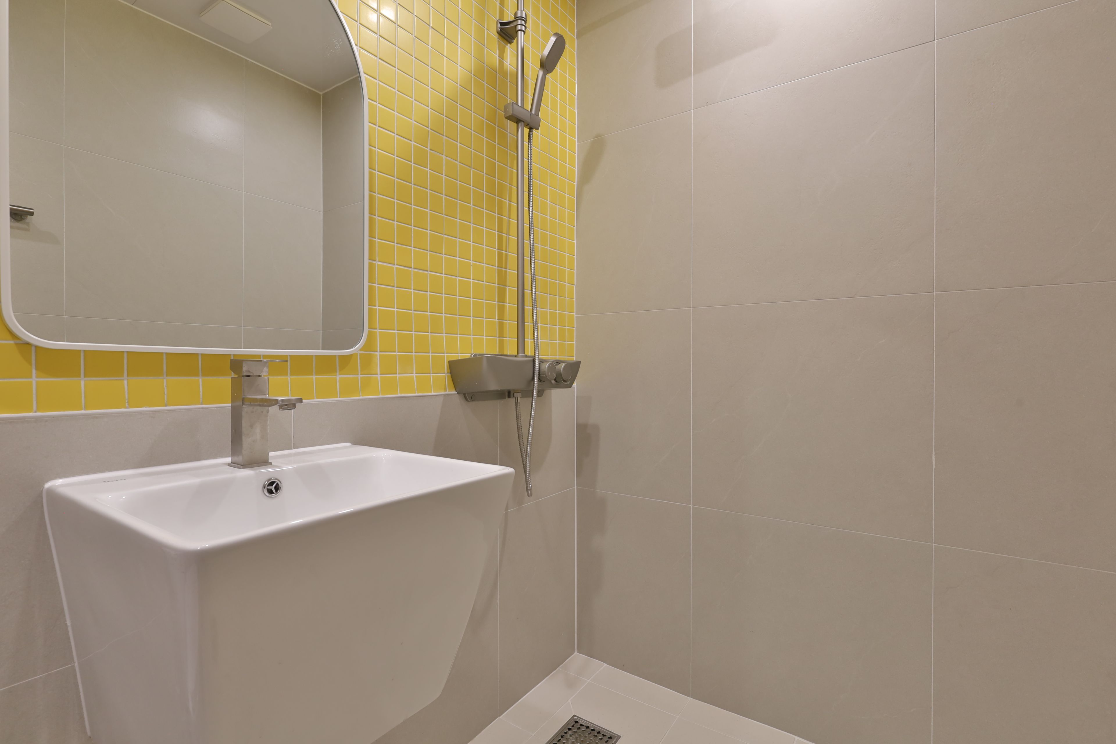 A bathroom with a white sink, a mirror, and a shower with a yellow-tiled wall.