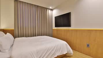 Habitación de hotel con cama, cortinas, televisor montado y cabecera de madera.