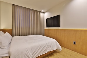 A hotel room with a bed, curtains, a mounted television, and a wooden headboard.