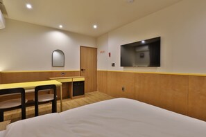 Una habitación de hotel con una cama, un escritorio con silla, un televisor montado en la pared y una puerta.