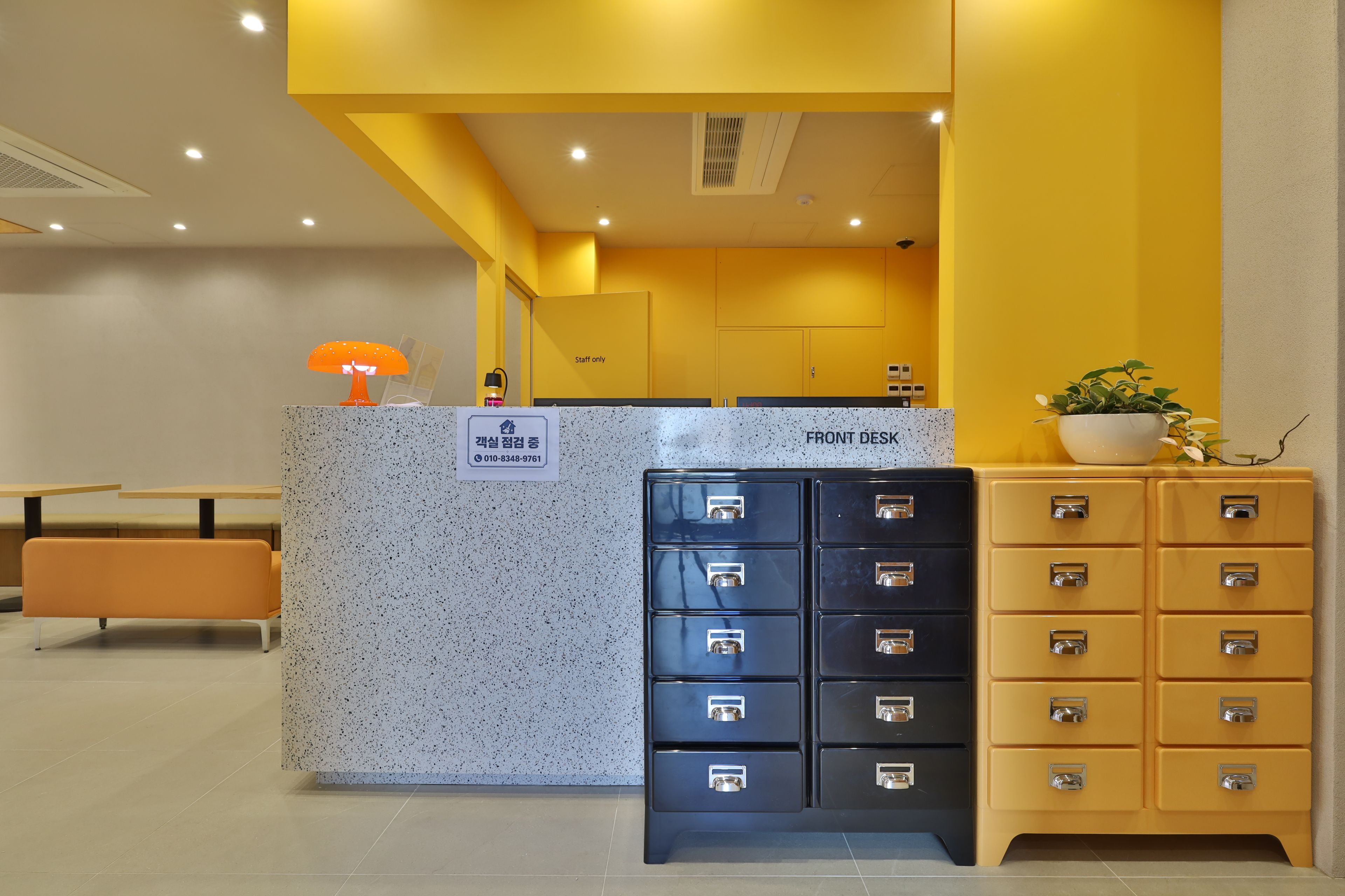 A reception desk with a 'Staff only' sign, a phone, and a plant. There are two chairs and a table in the background.