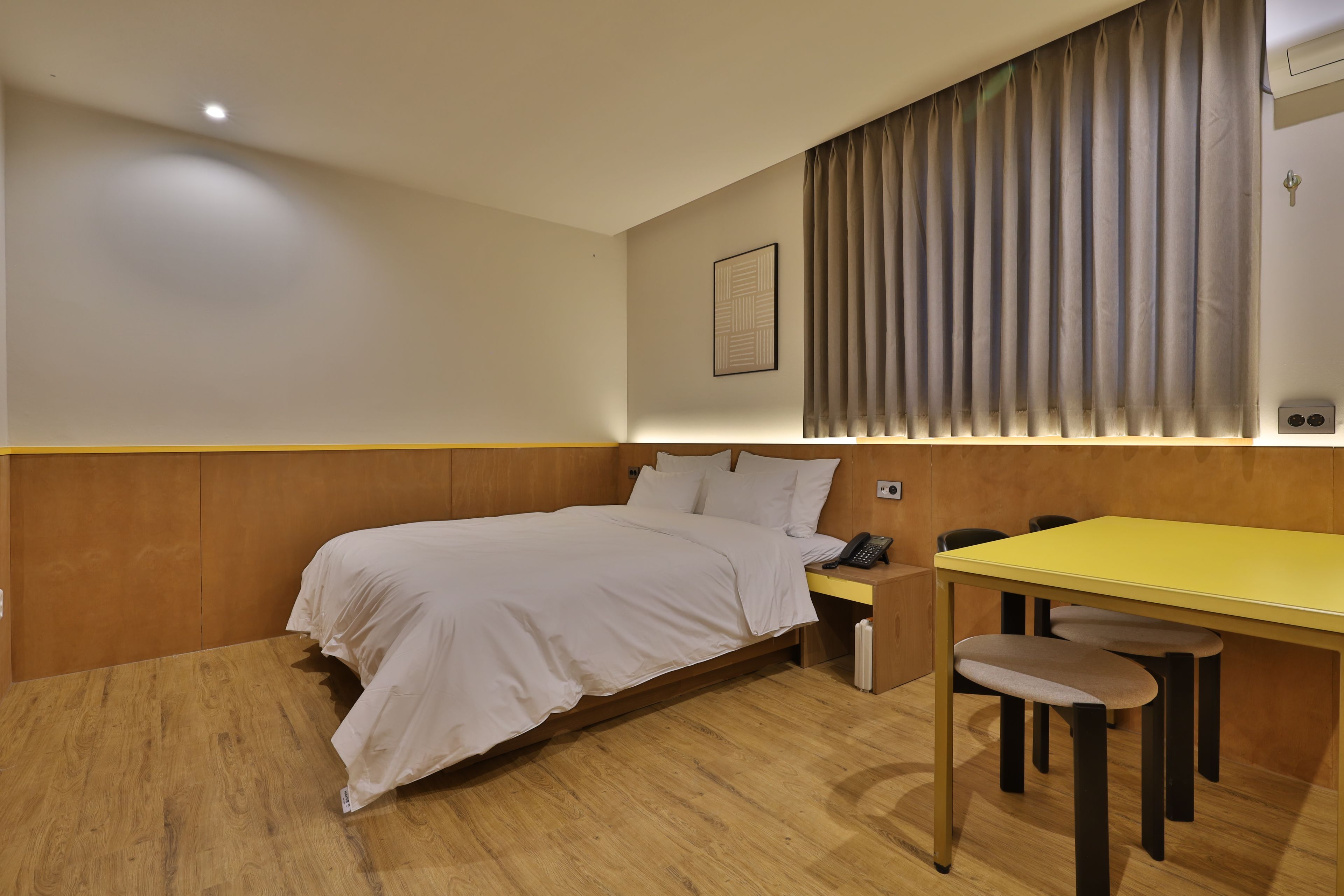 A hotel room with a bed, bedside table, and a desk with chairs.