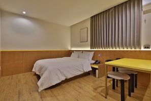 A hotel room with a bed, bedside table, and a desk with chairs.