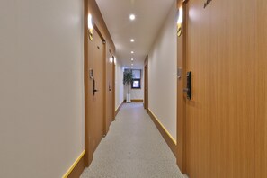 A hotel hallway with wooden doors, a carpeted floor, and a plant in the distance.