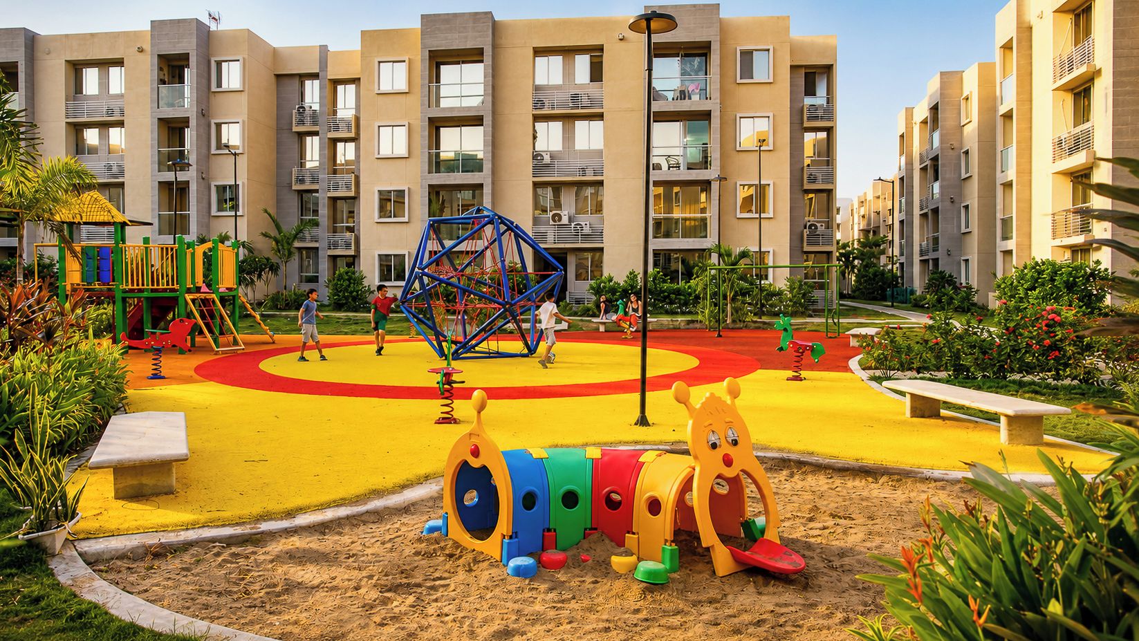 Une aire de jeux avec des équipements colorés et un espace de jeux sablonneux, le tout entouré d’un bâtiment doté de balcons.
