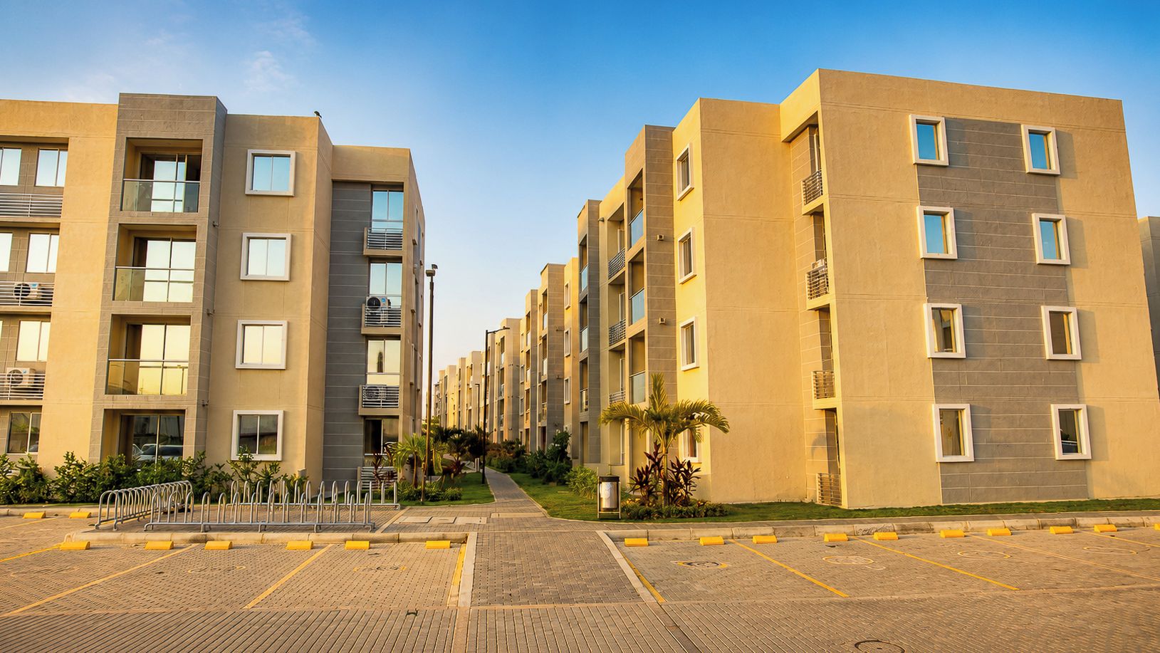 Un immeuble d’appartements moderne, doté de plusieurs étages, de balcons et d’un espace de stationnement dallé.