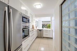 A modern kitchen with stainless steel appliances, white cabinetry, and a view of the outdoors through a window. - Kananda Riverside, Noosa Heads (Noosa Heads)