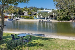 A lakeside view with a dining area, boats, and buildings in the background. - Kananda Riverside, Noosa Heads (Noosa Heads)