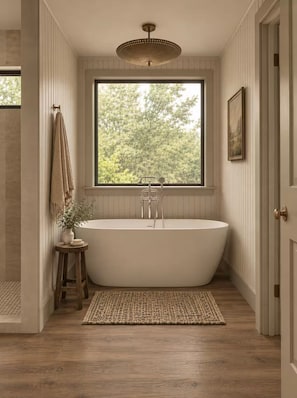 A modern bathroom with a freestanding bathtub, a large window with a view of trees, and a wooden floor.